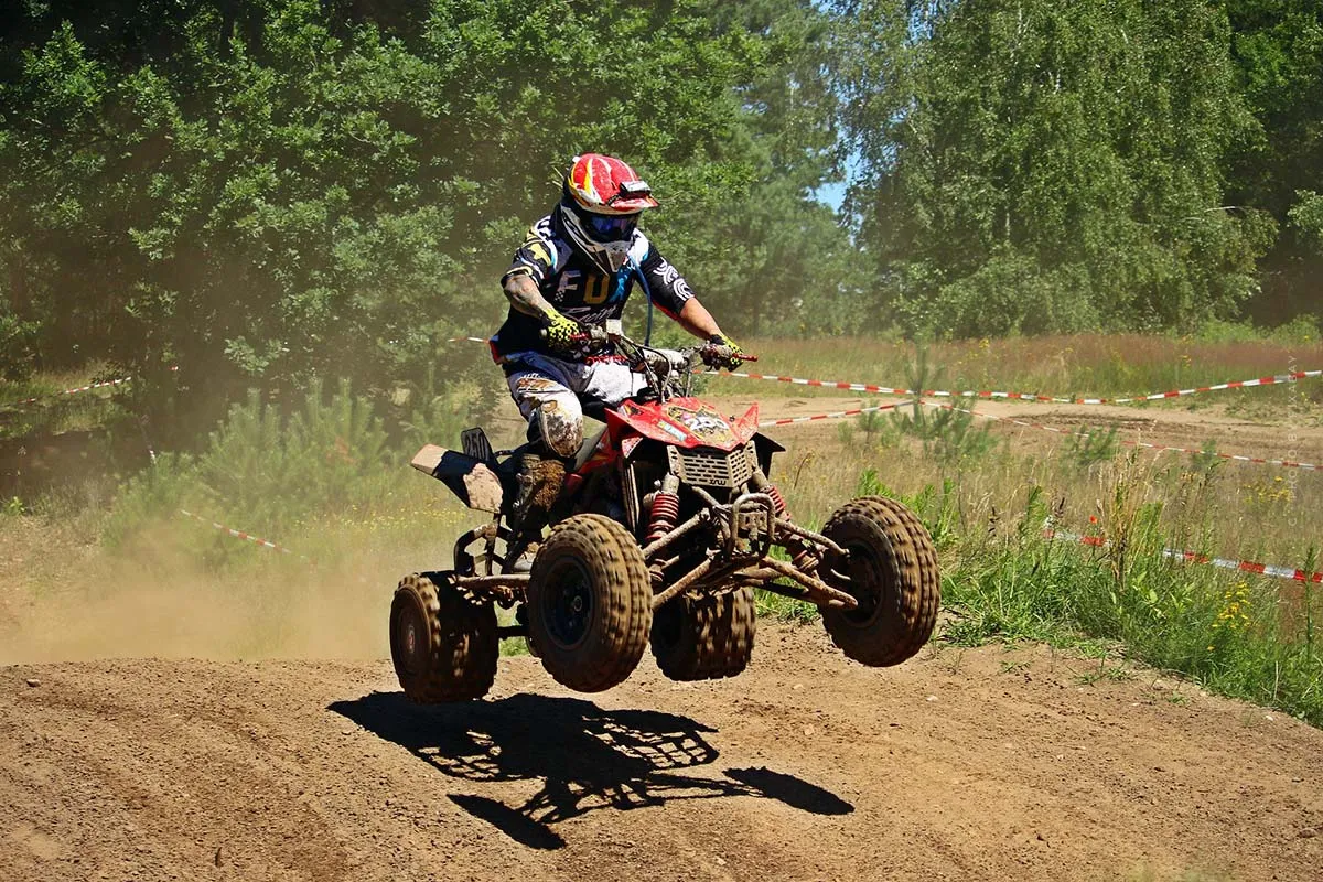 Quad springt über eine Geländekuppe im Staub